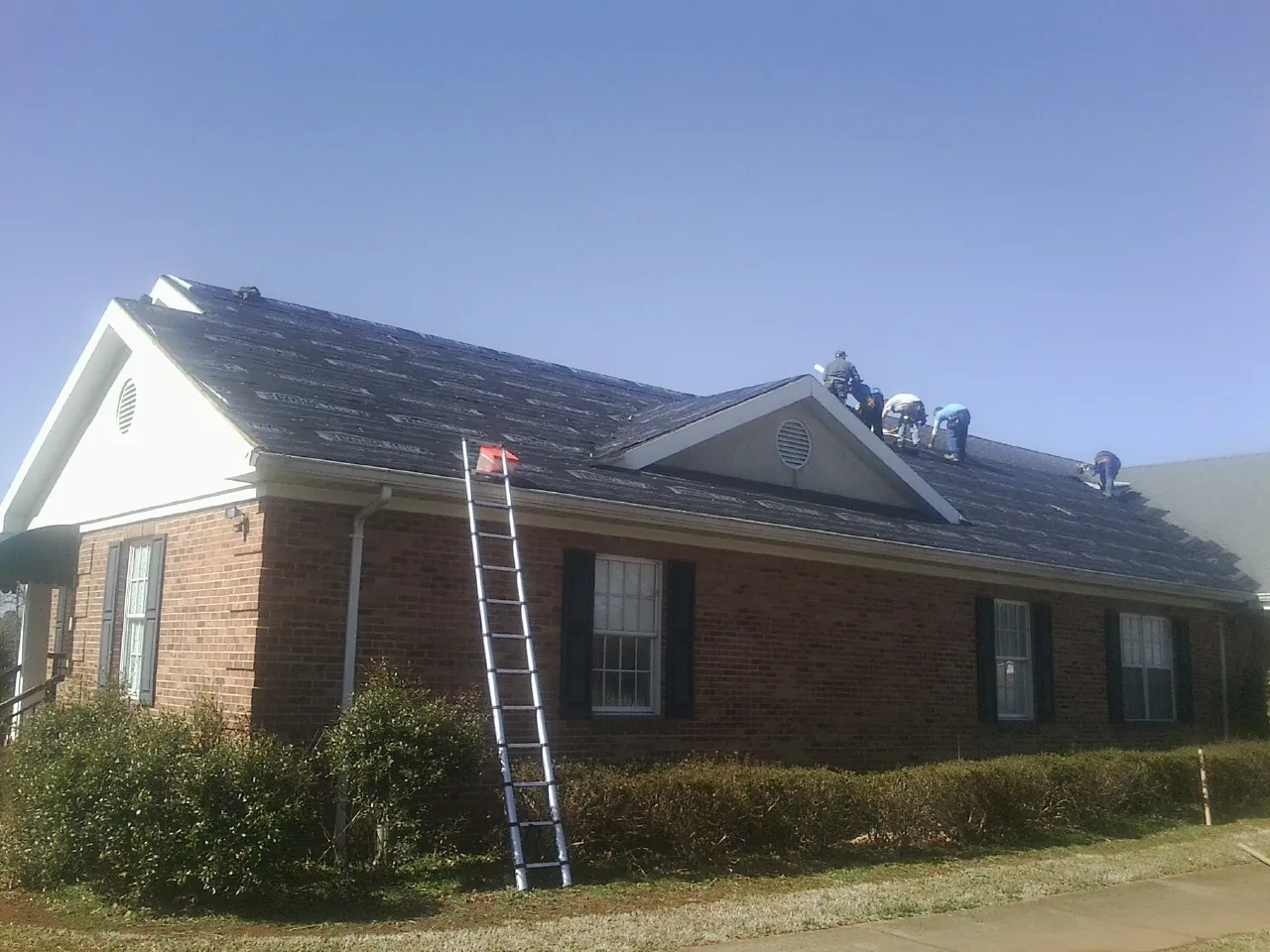Crew tearing shingles off a brick ranch roof with a ladder set — Metal Roof Repair work by our crew in Ellenville