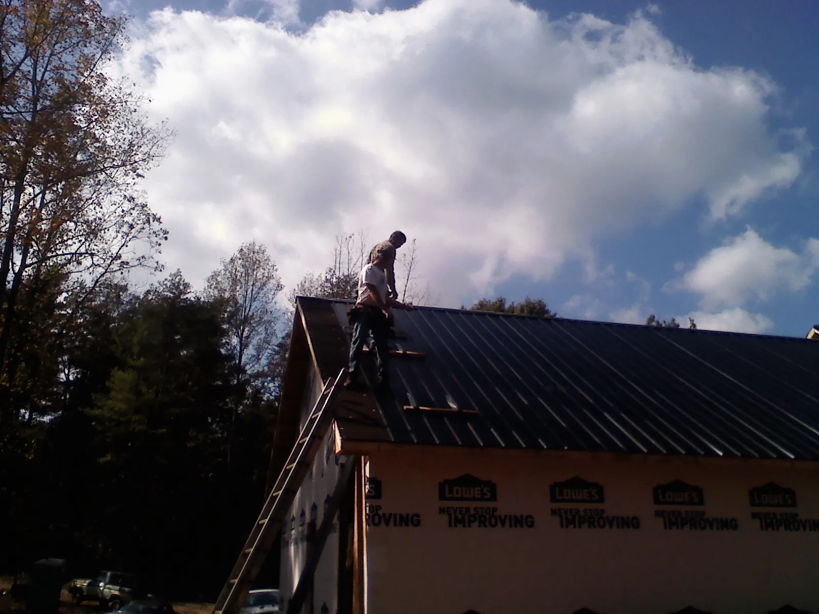 Roofer fastening dark metal panels high against a cloudy sky, from a Roof Inspection job in Ellenville