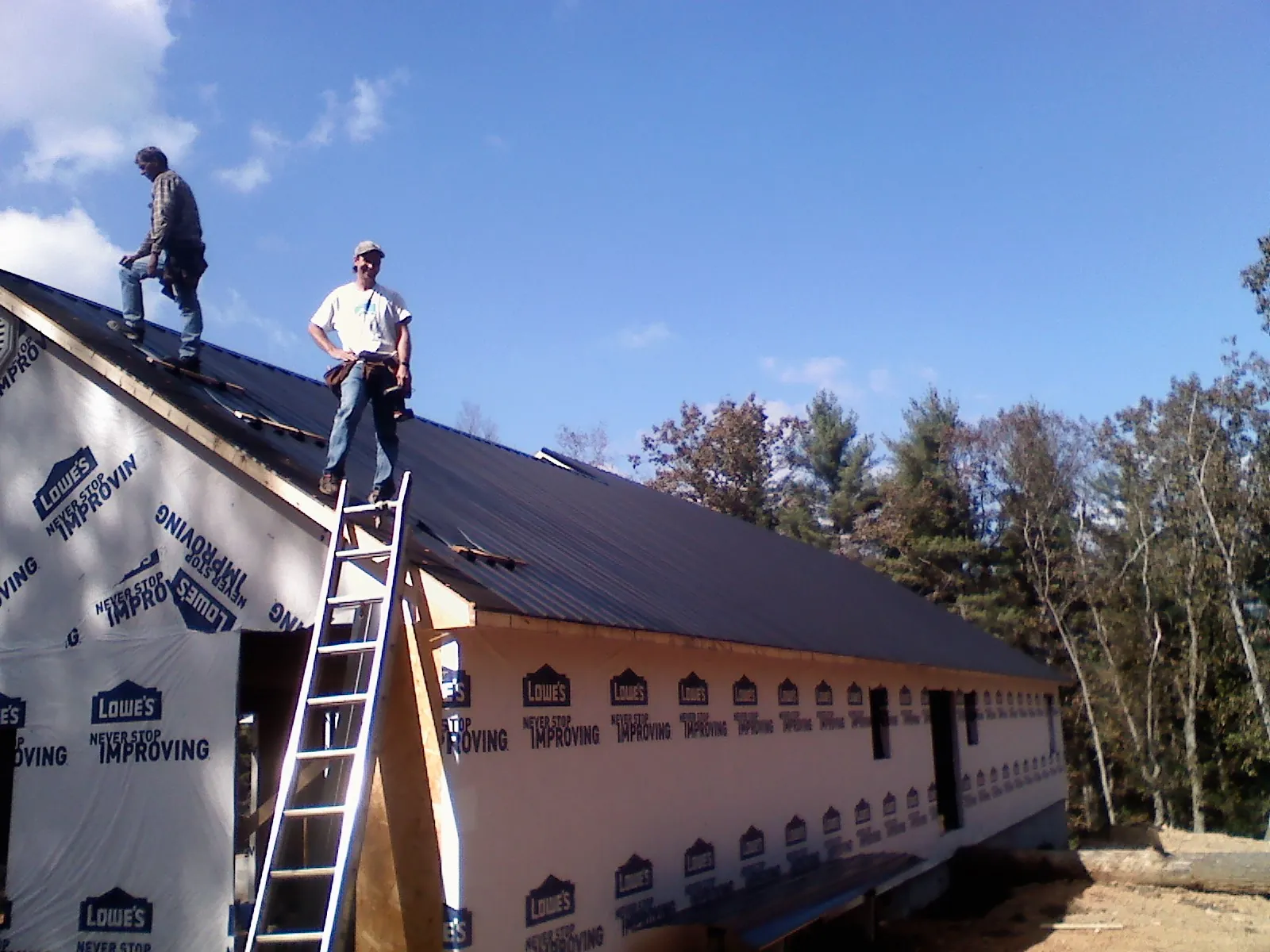 Two roofers standing on a long dark metal roof over a wrapped building in Ellenville