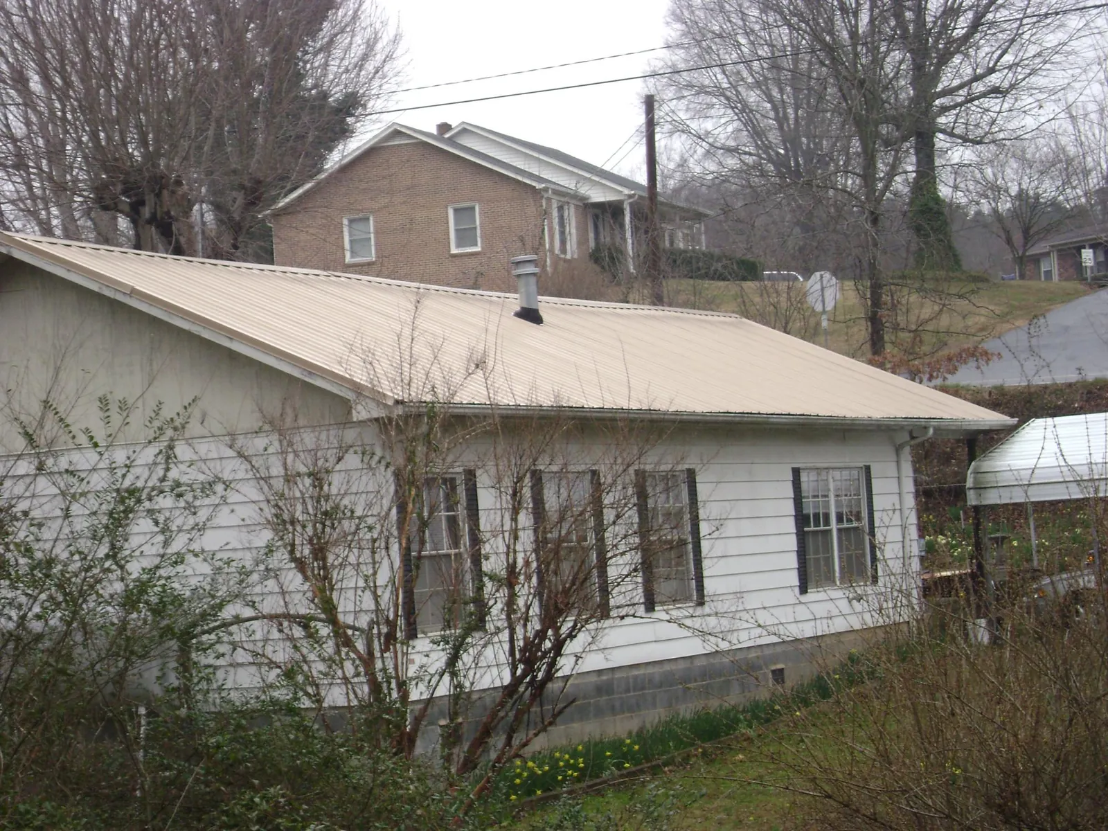 Tan metal roof on a white sided house set into a hillside — Commercial Roofing by Roofing Brothers in Ellenville